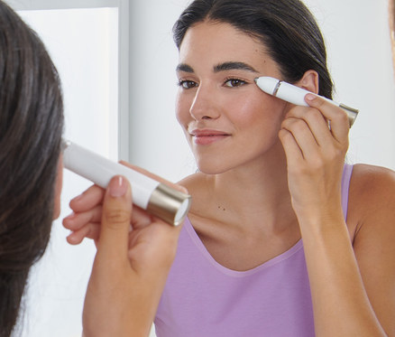 Žena si upravuje obočí elektrickým zastřihovačem obočí před zrcadlem.