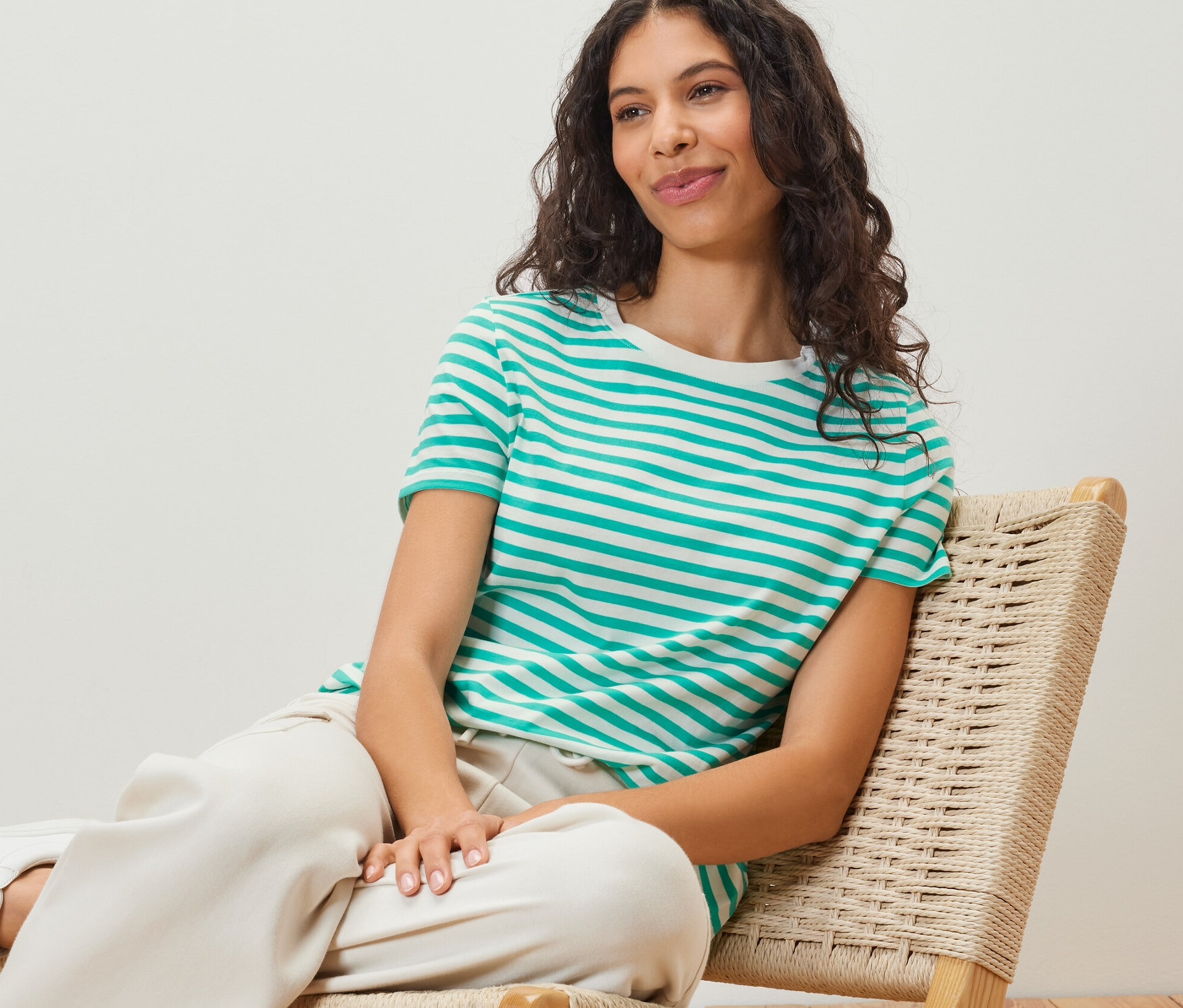 Žena sedí na židli a má na sobě tričko se zelenými a bílými proužky.