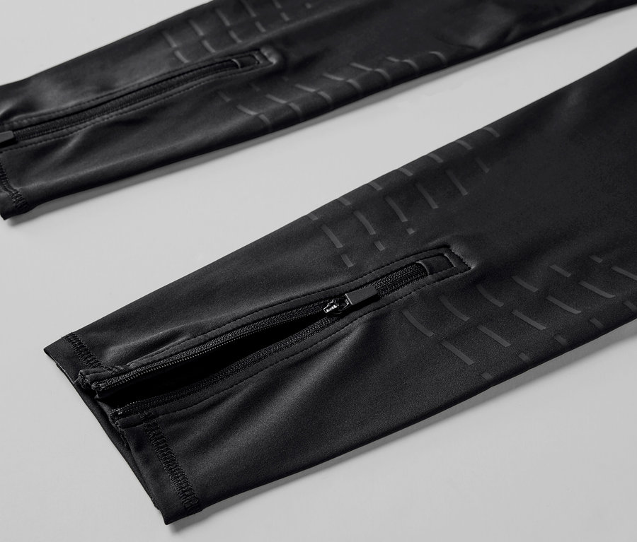 Detailní pohled na černé běžecké legíny se zipy na nohavicích.