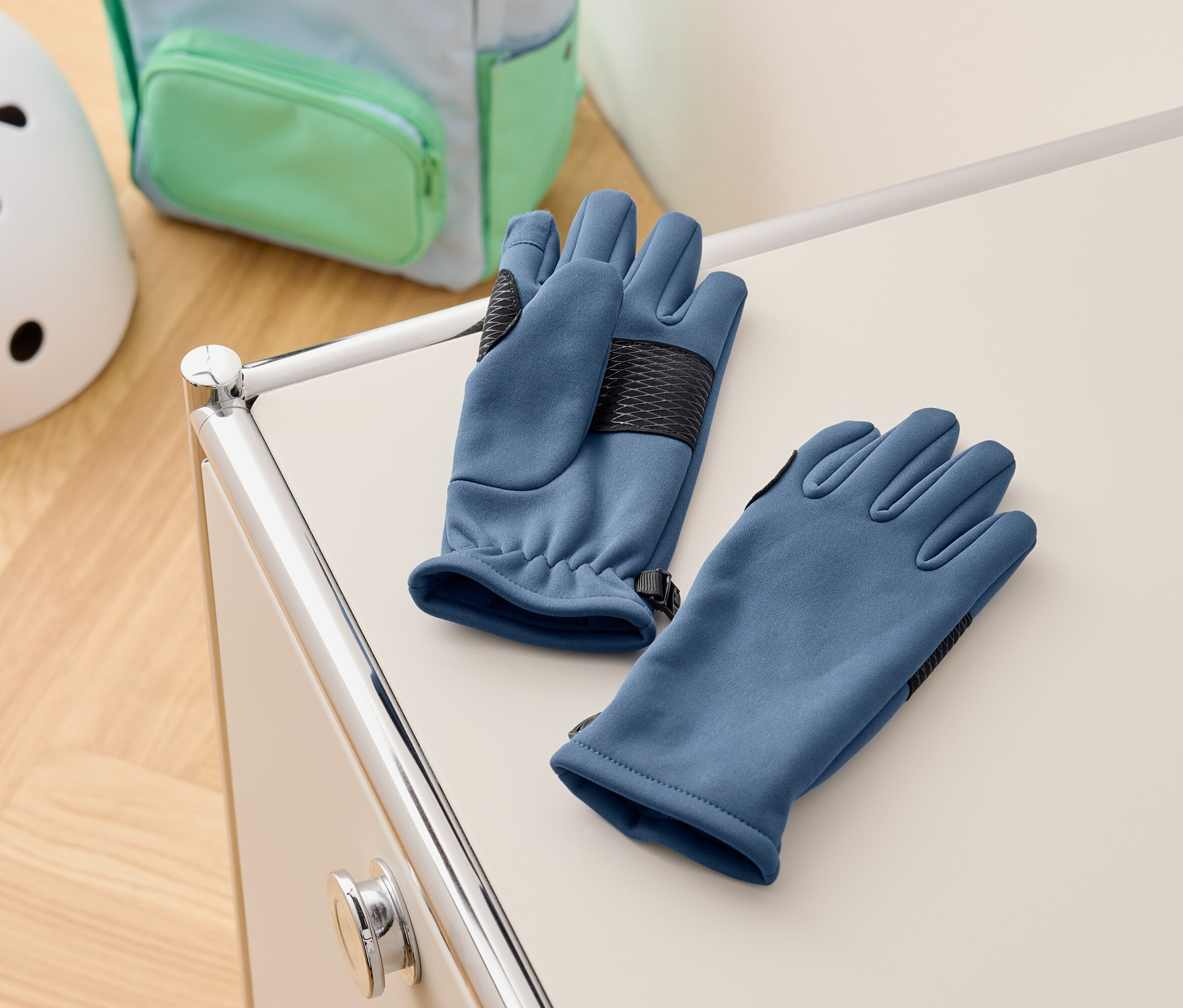 Modré rukavice leží na bílé skříňce, v pozadí je batoh a helma.