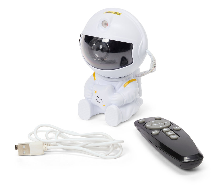 Bílý projektor noční oblohy ve tvaru astronauta sedí vedle černého dálkového ovladače a bílého USB kabelu.