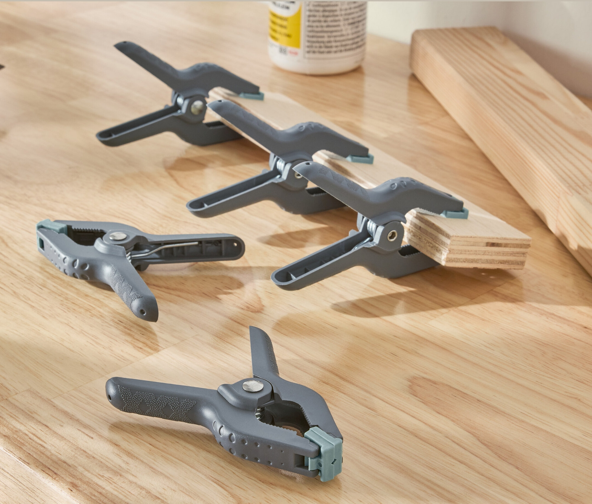 Na dřevěném povrchu leží vrtačka a pět šedých klempířských svěrek.