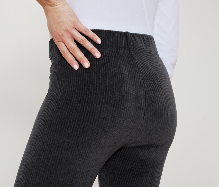 Žena v šedých manšestrových kalhotách si položí ruku na bok.