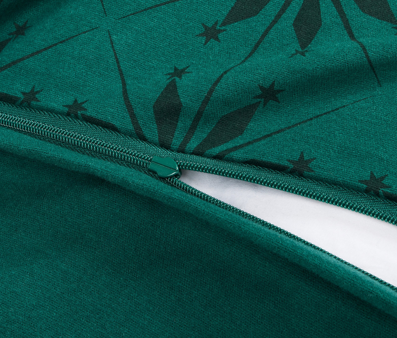 Detailní pohled na rozepnutý zip na zeleném povlečení s tmavě zeleným geometrickým vzorem.