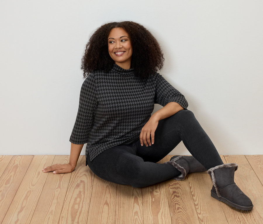 Žena sedí na podlaze a má na sobě manšestrové legíny, top se vzorem a boty.