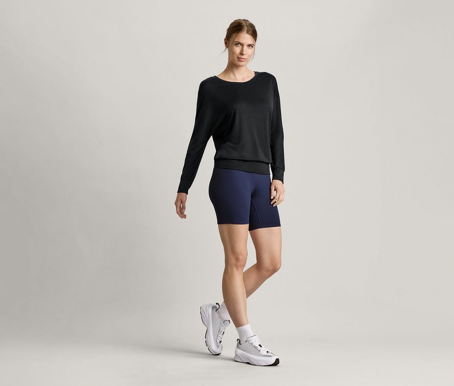 Žena má na sobě černé sportovní triko na jógu a krátké sportovní legíny.