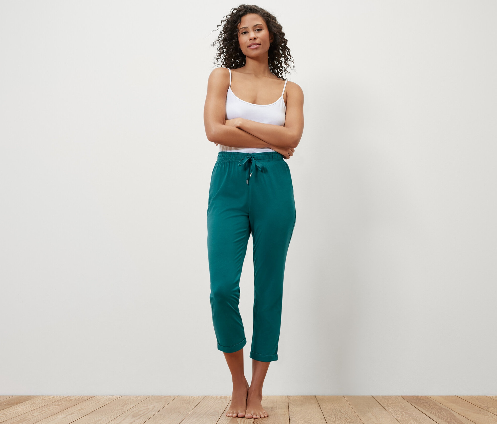 Žena stojí s rukama zkříženýma na prsou a má na sobě zelené pyžamové kalhoty.