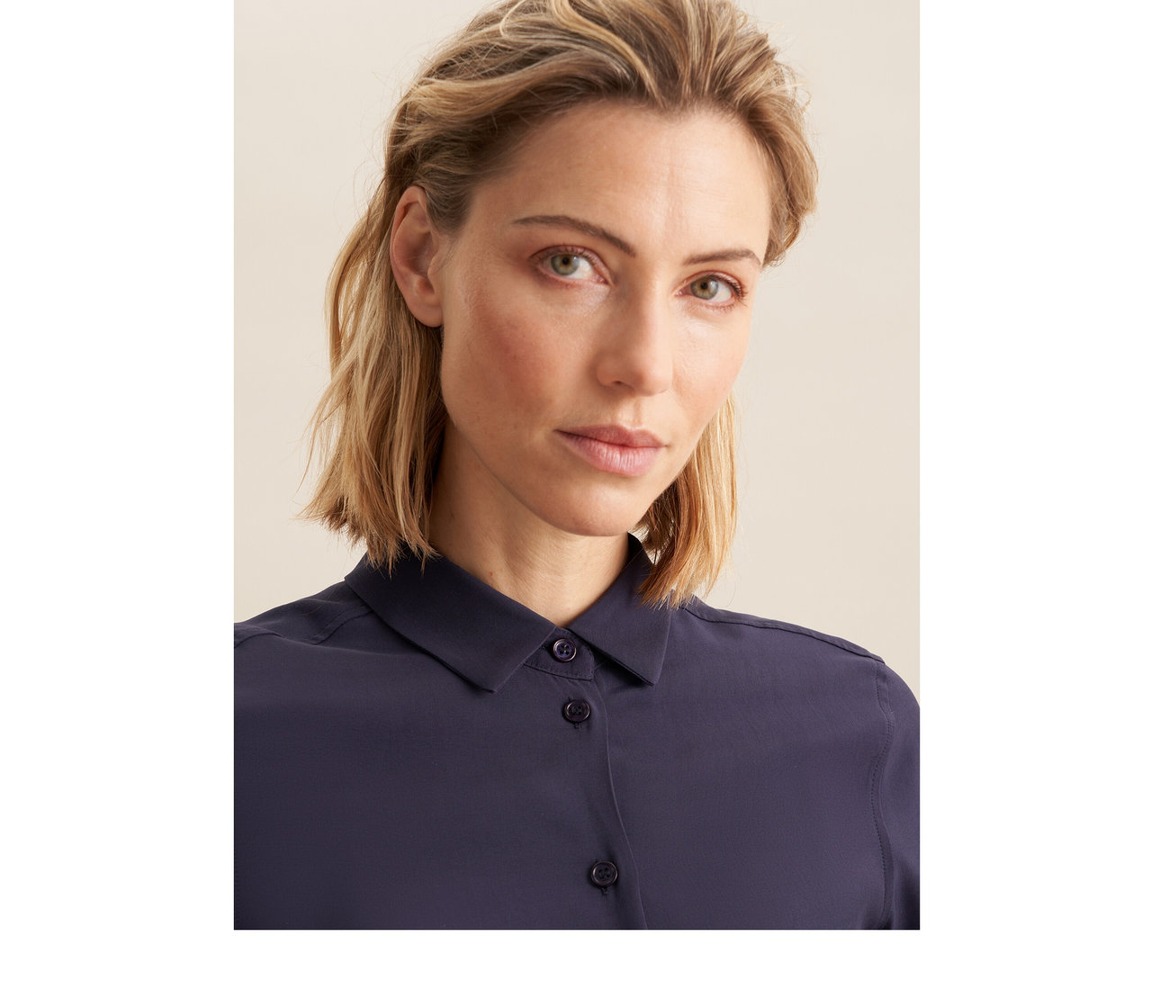 Žena s krátkými blond vlasy v tmavomodré halence z viskózy Seidensticker, dívá se přímo do kamery.