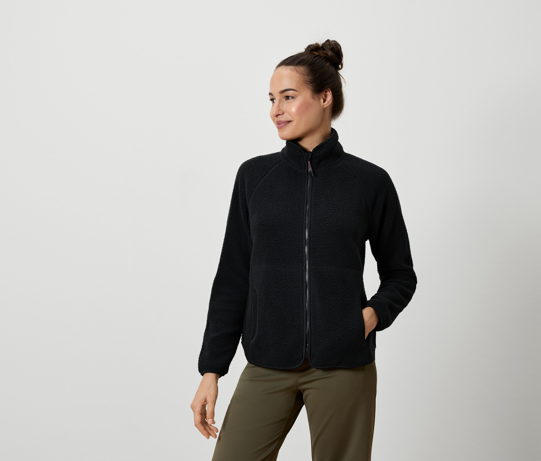 Žena má na sobě černou fleecovou bundu a olivově zelené kalhoty.