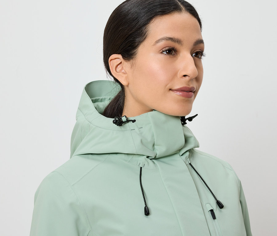 Žena má na sobě světle zelenou bundu s kapucí.