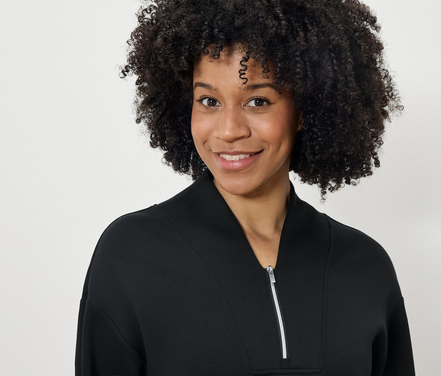 Portrét usmívající se ženy s afro účesem v černé mikině na zip.