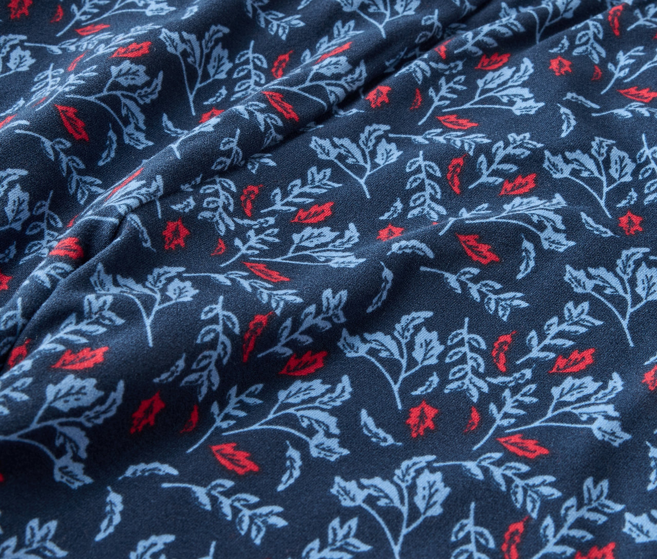 Detailní záběr na tmavě modrou látku s potiskem červených a světle modrých listů.