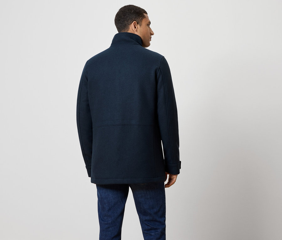 Muž zády, má na sobě tmavě modrý kabát a džíny.