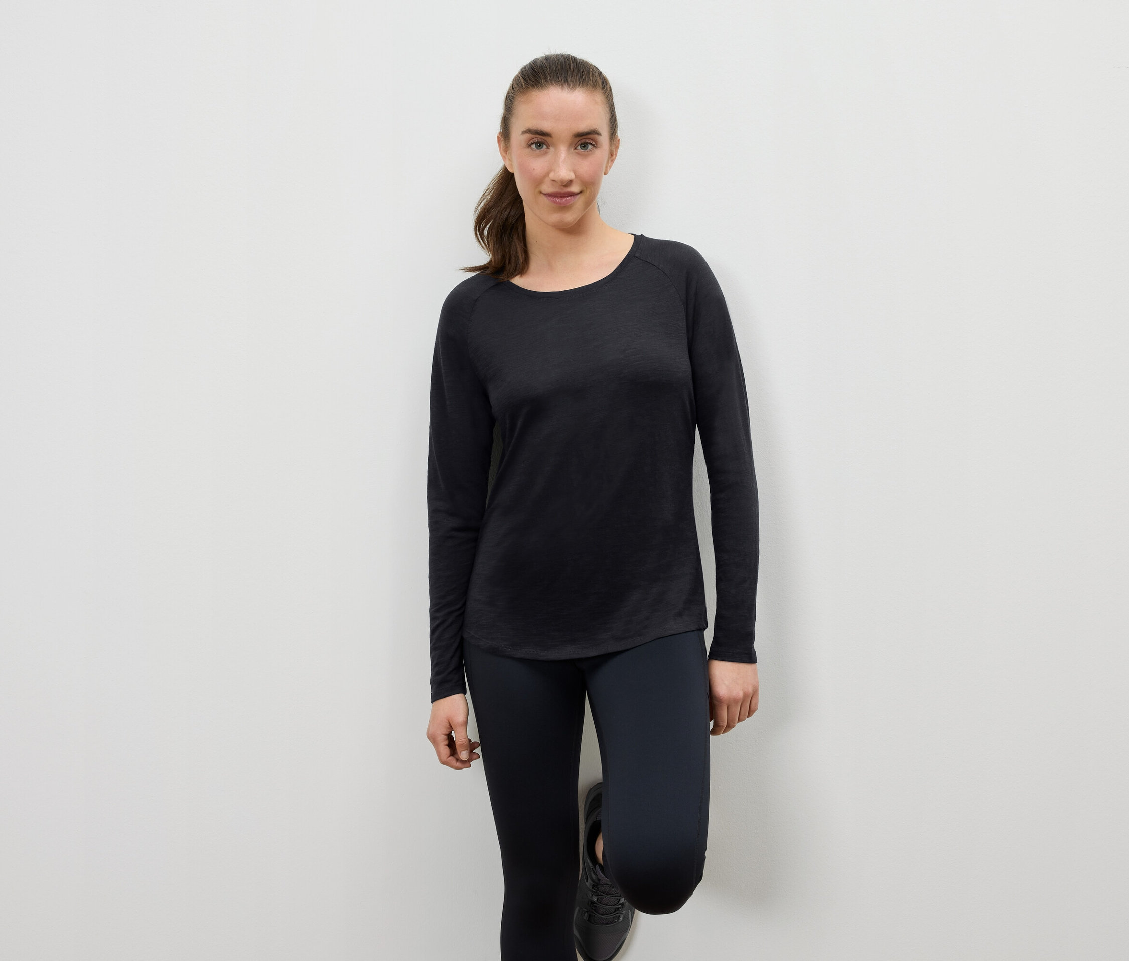 Žena v černém sportovním oblečení opřená o zeď.