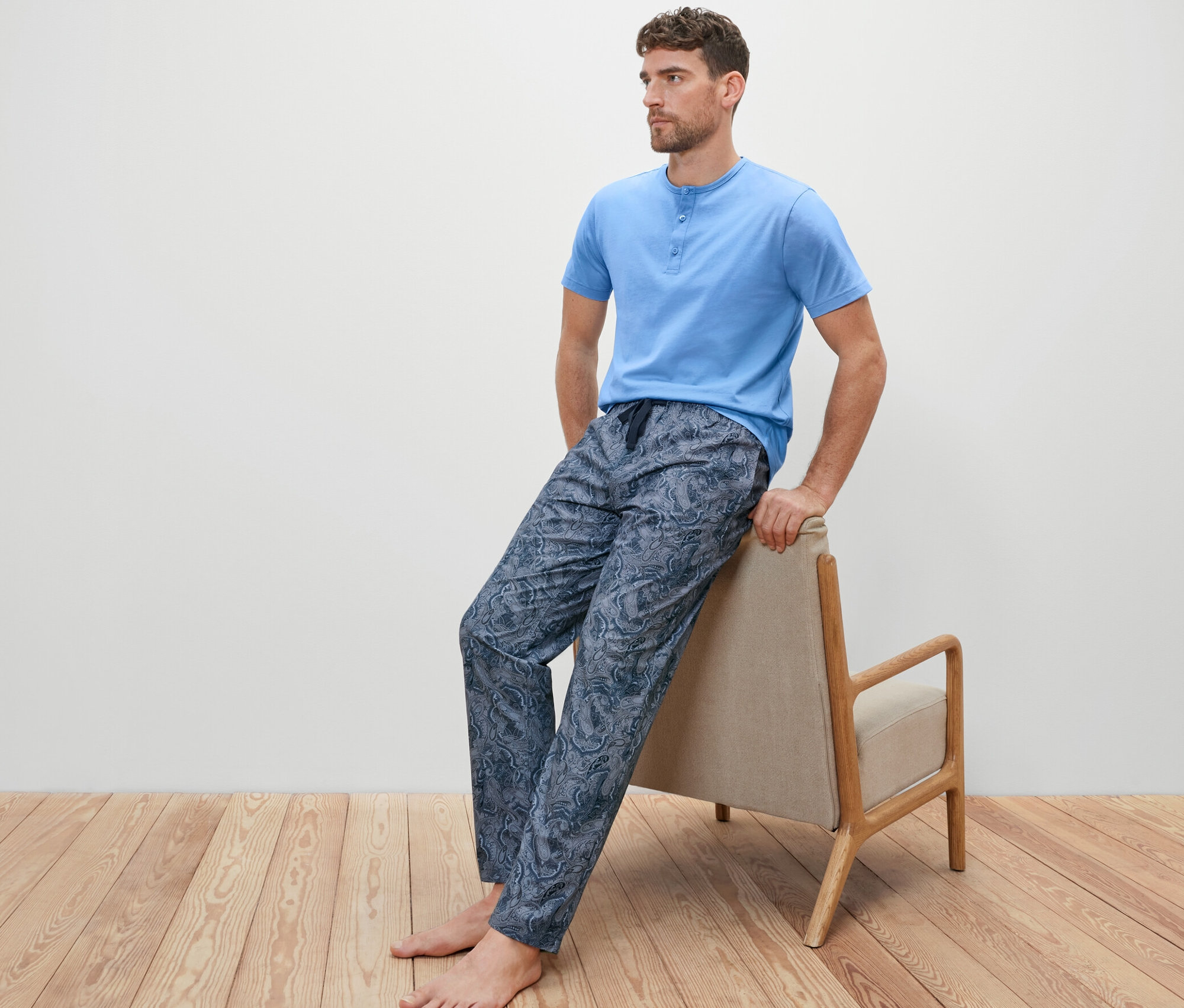 Muž sedí na křesle a má na sobě pyžamovou soupravu s tkanými kalhotami.