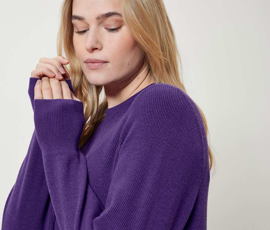 Blondýna v purpurovém svetru si dává ruce k obličeji.