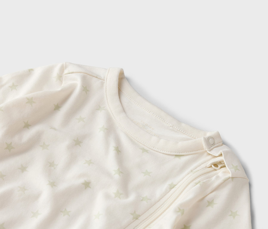 Detailní záběr světlého dětského overalu se vzorem hvězdiček, zipem a knoflíkem u krku.