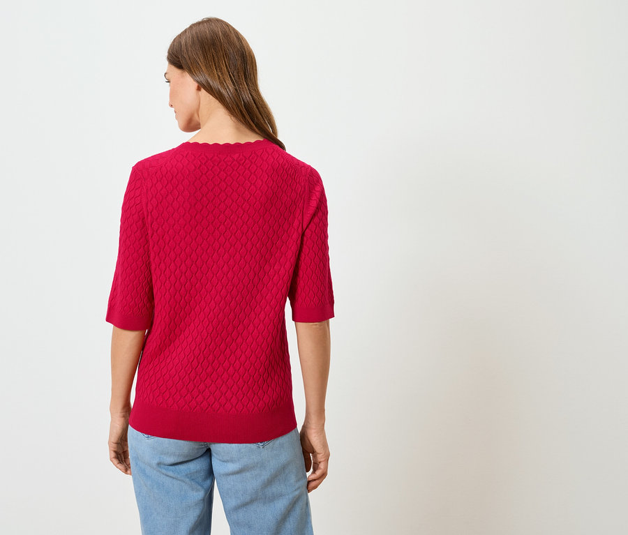 Pohled zezadu na ženu s dlouhými hnědými vlasy v červeném svetru a modrých džínách.