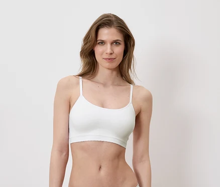 Žena má na sobě bílou sportovní podprsenku na bílém pozadí.