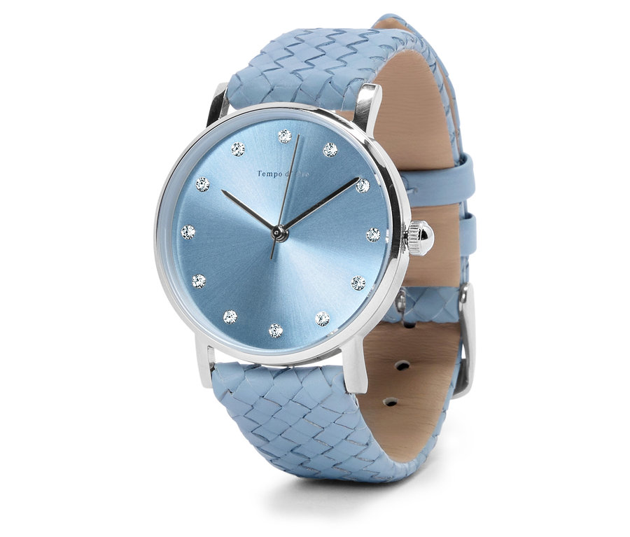 Detailní záběr na náramkové hodinky se světle modrým ciferníkem, stříbrným pouzdrem a světle modrým, pleteným řemínkem.