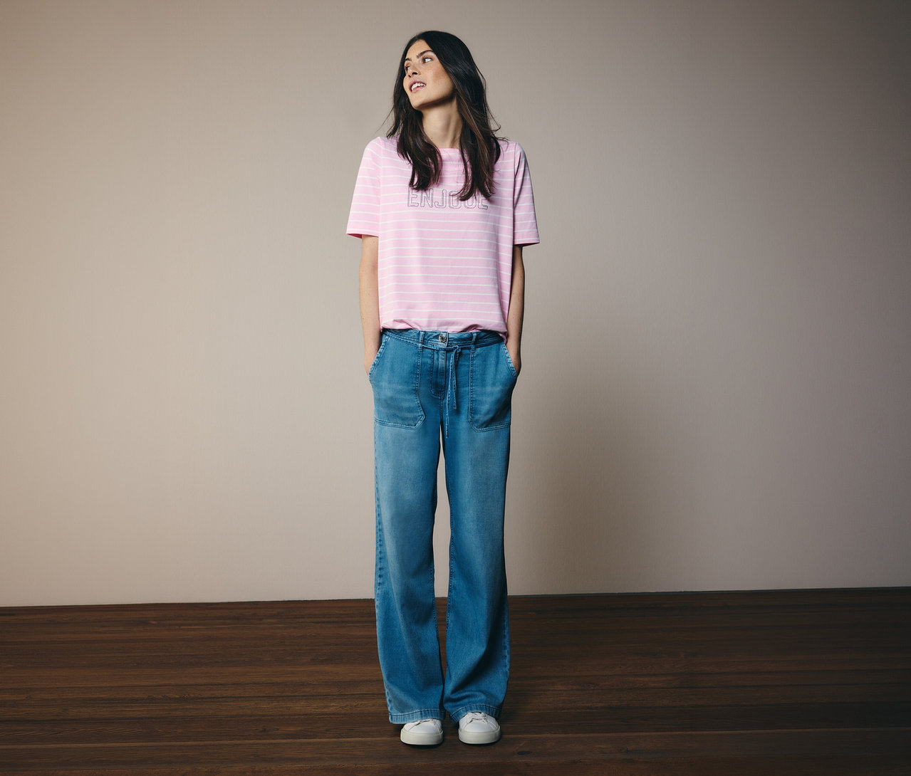 Žena s rukama v kapsách nosí tričko CECIL s růžovými pruhy a džíny.