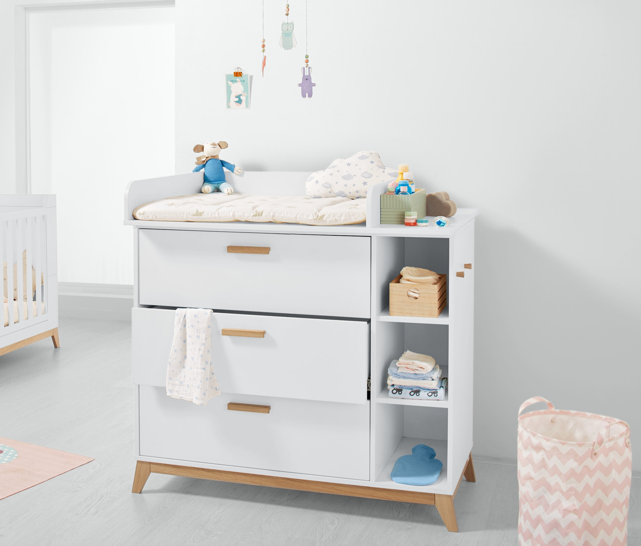 Bílá přebalovací komoda se třemi zásuvkami a otevřenými policemi.