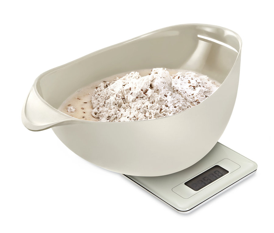 Béžová mísa na pečení chleba s těstem stojí na digitální váze.