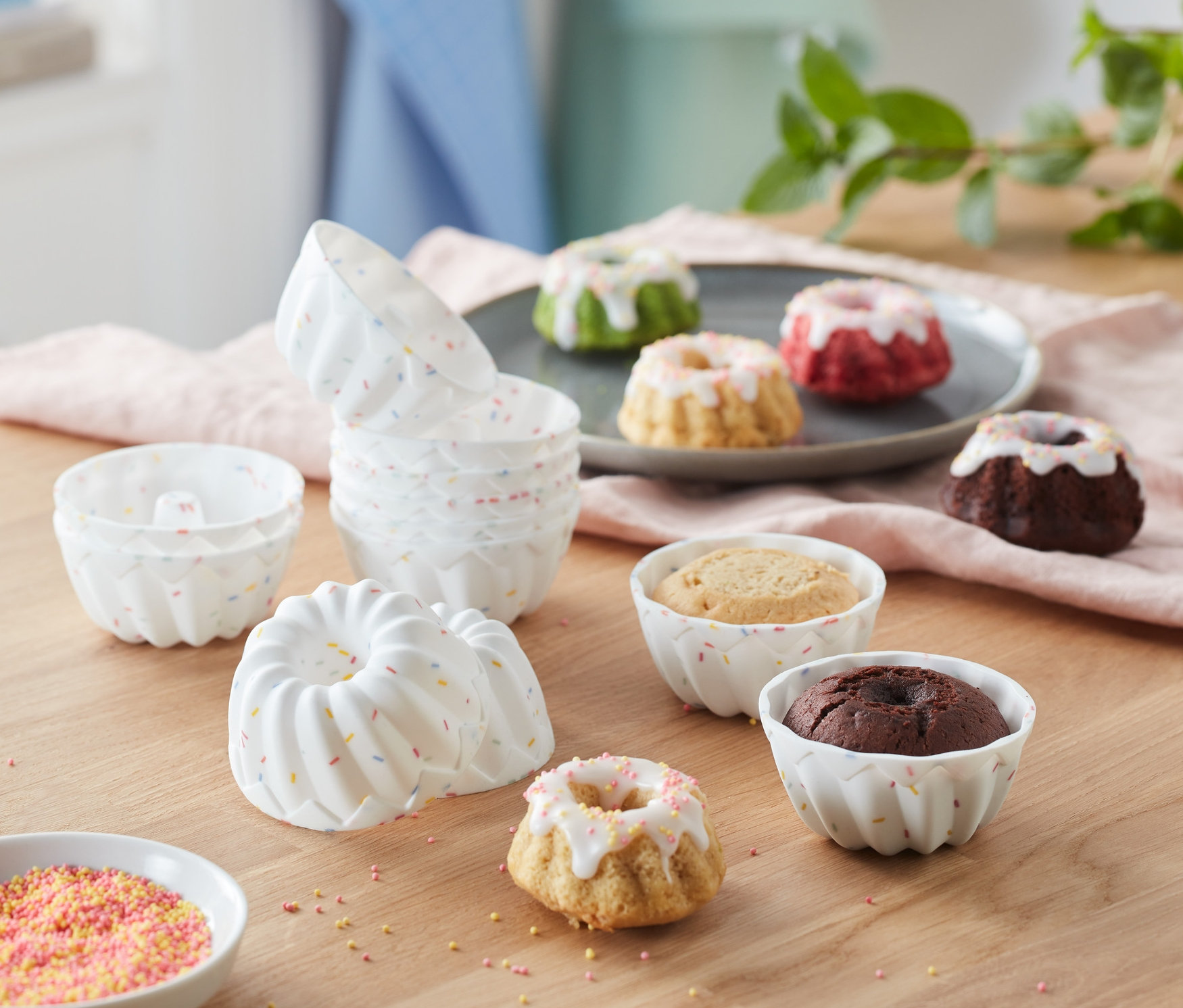 Formičky na minibábovky, 12 ks, jsou na stole s mini bábovkami různých barev.