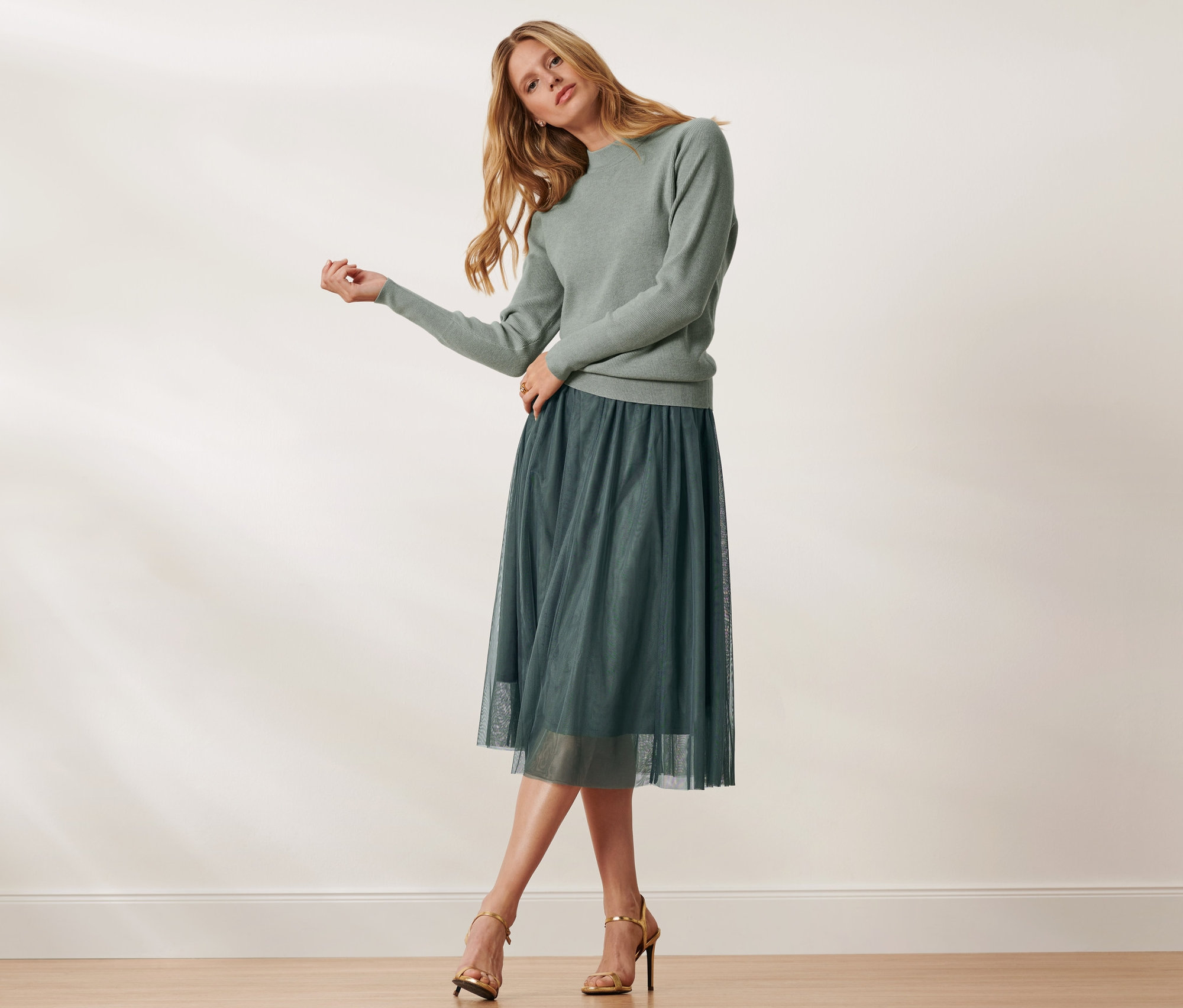 Žena pózuje v zeleném svetru a tylové sukni.