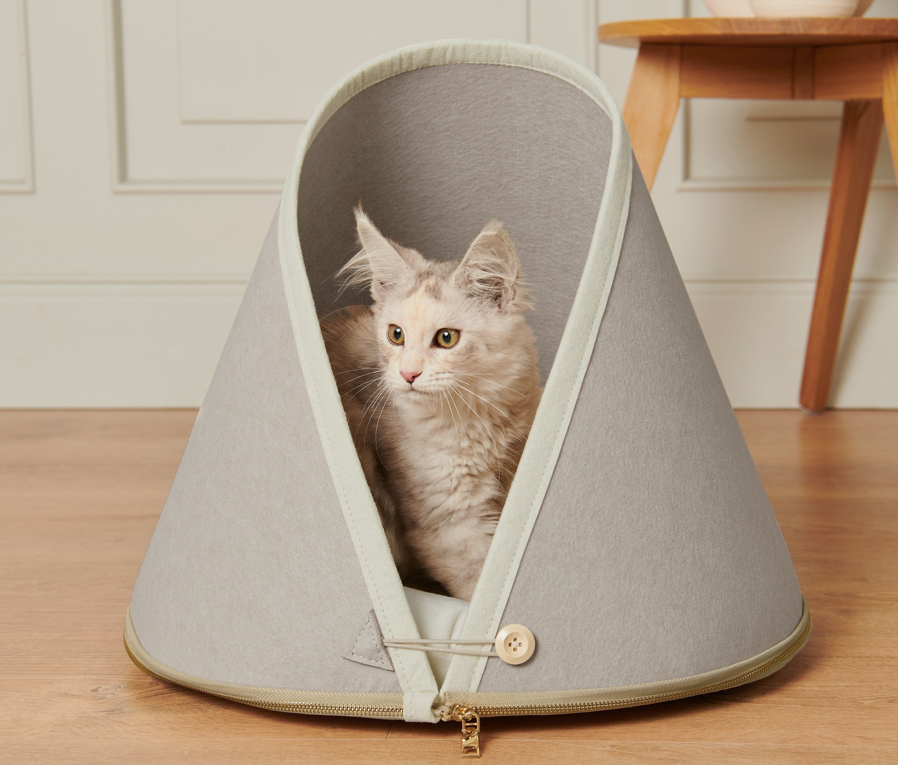 Kočka leží v šedém pelíšku s polštářkem.