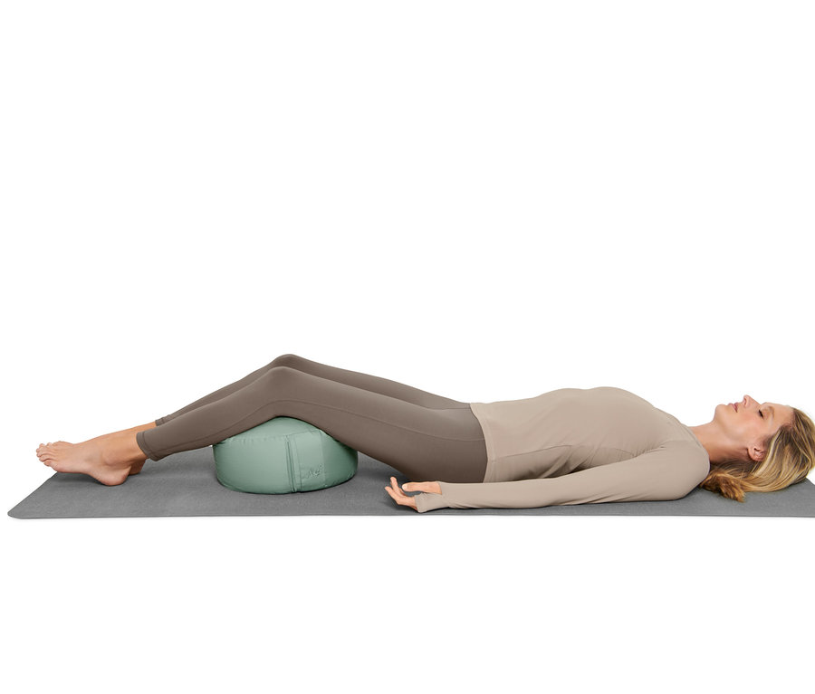 Žena leží na podložce a pod zády má meditační polštářek.