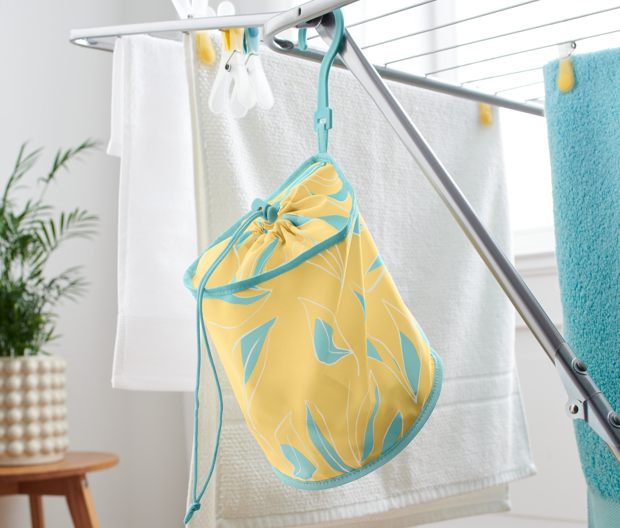 Žlutý sáček na kolíčky na prádlo s modrým lemováním visí na sušáku na prádlo.