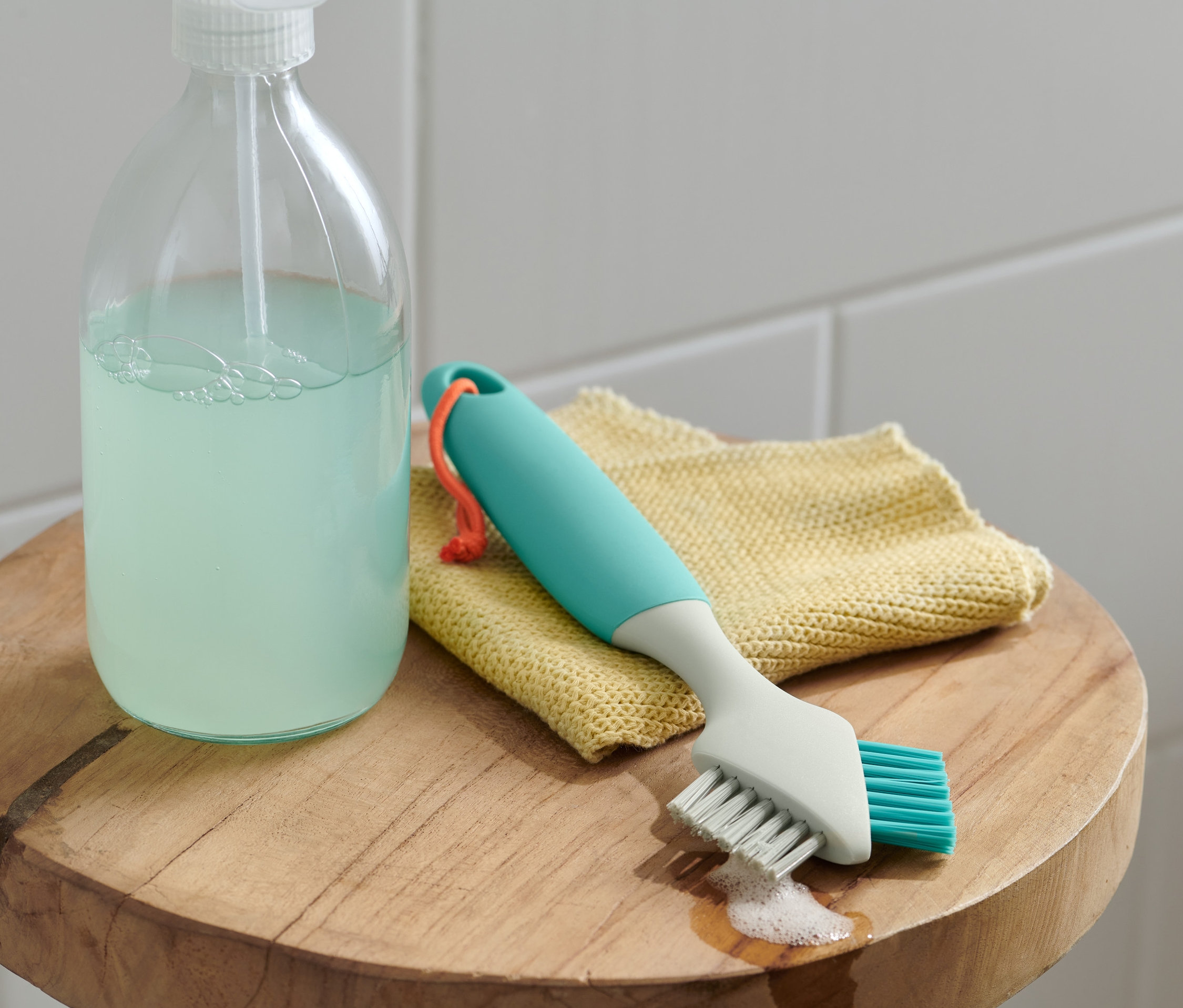 Kartáč na čištění spár, měkký/tvrdý leží na žluté utěrce vedle čisticího prostředku.