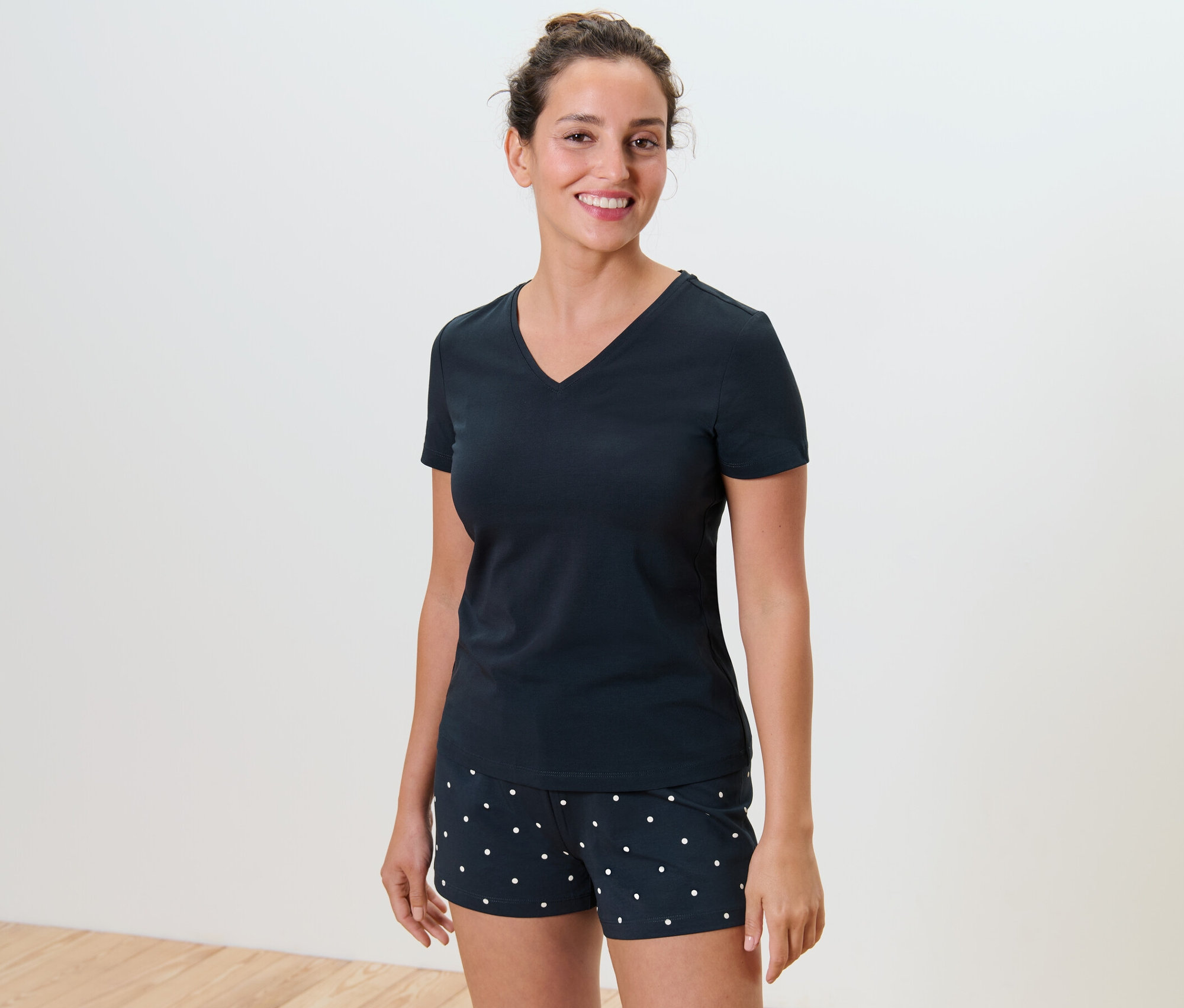 Usmívající se žena má na sobě krátké pyžamo s puntíky.