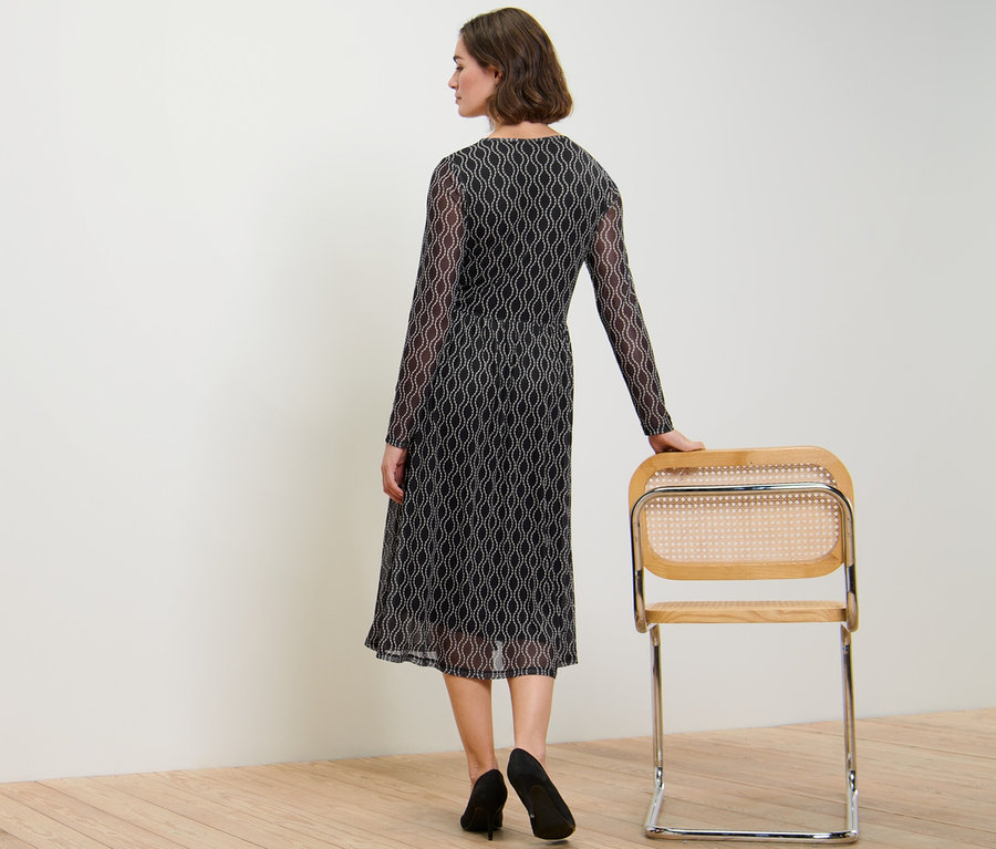 Žena stojí zády k fotoaparátu a má na sobě síťované šaty s potiskem.