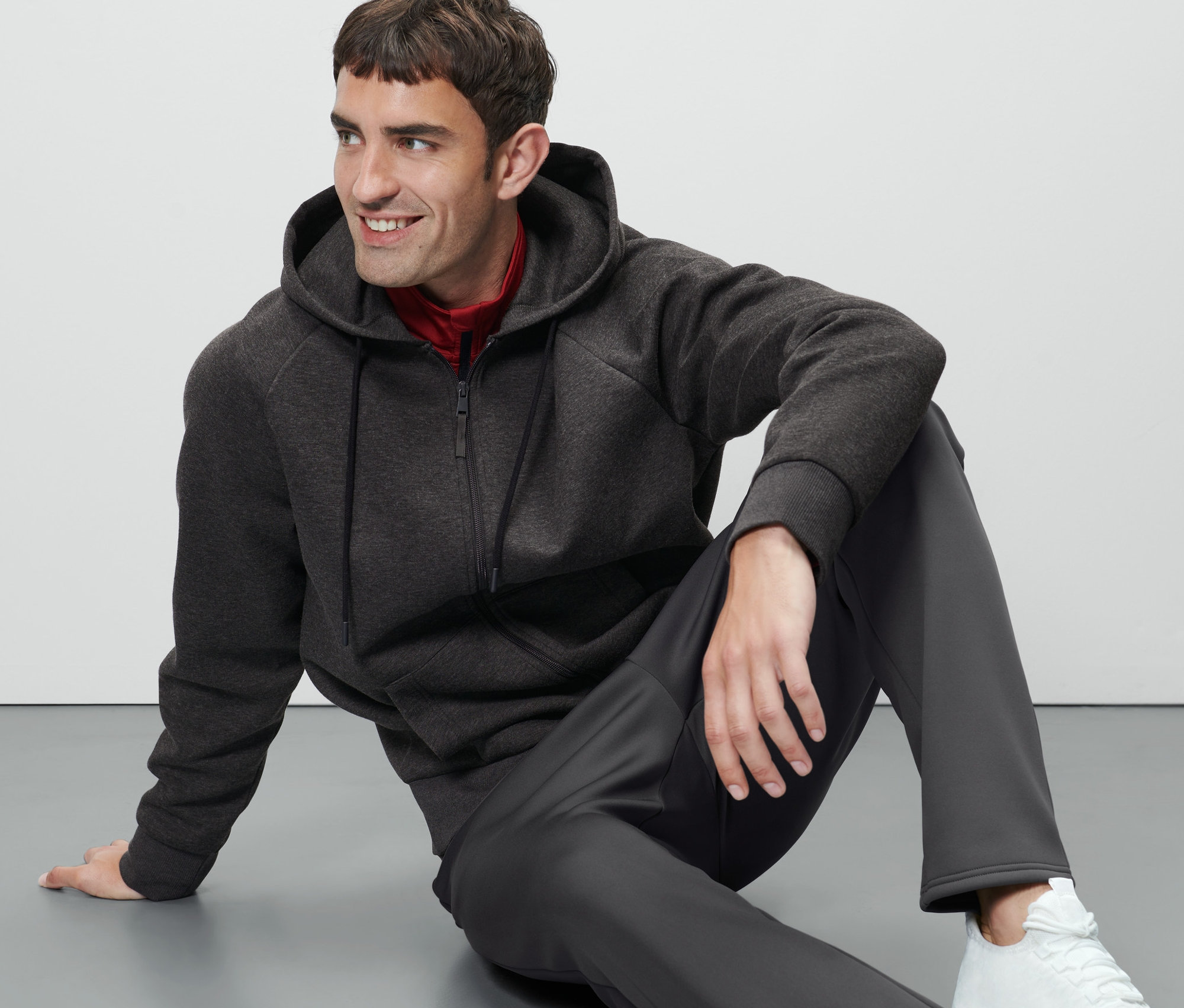 Muž sedí na zemi a má na sobě funkční bundu s kapucí.