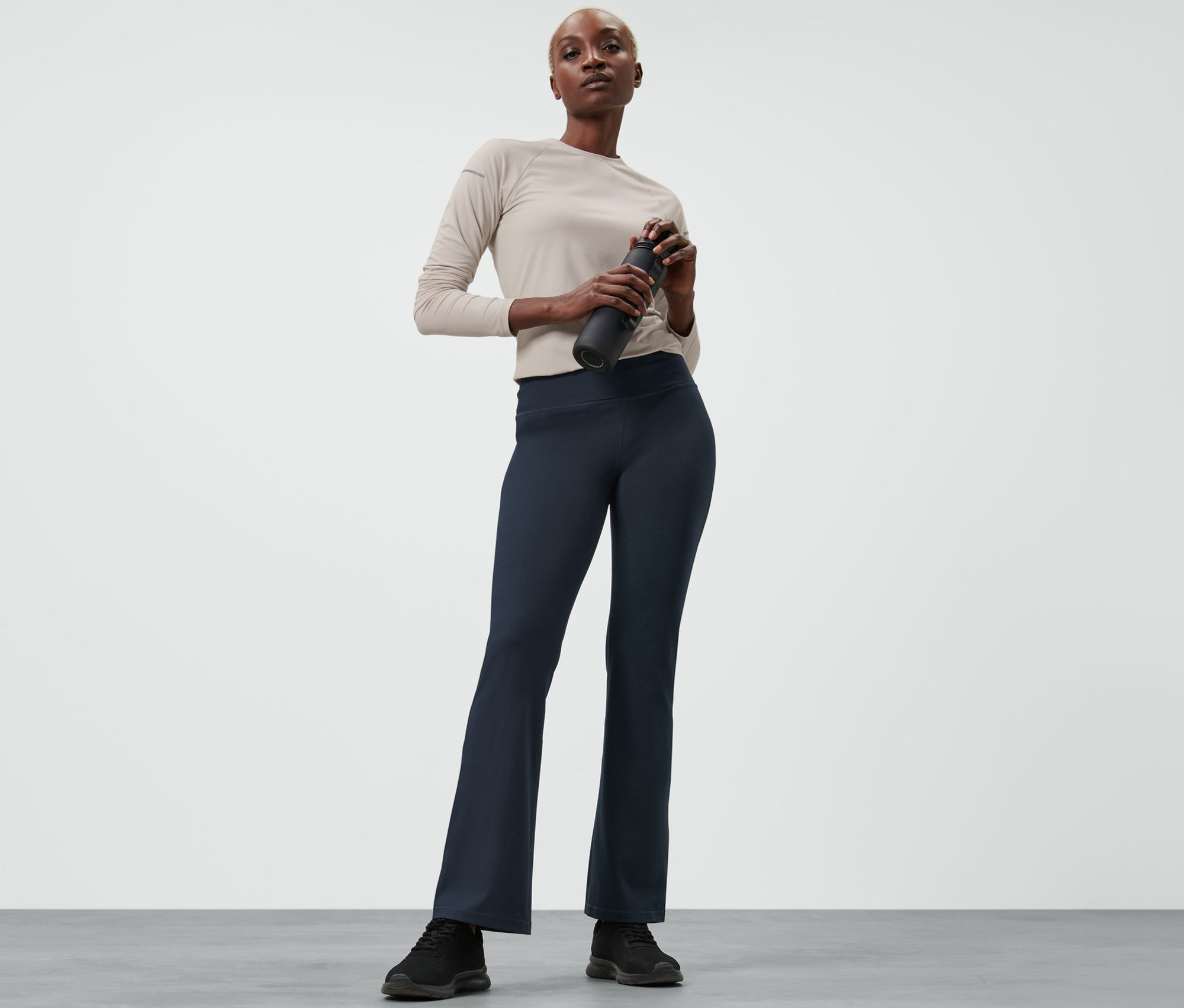 Žena drží láhev na vodu a má na sobě stahovací sportovní kalhoty.