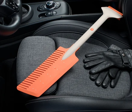 Oranžová autoškrabka na led Autoškrabka na led, zásuvná leží na sedadle auta vedle černých rukavic.