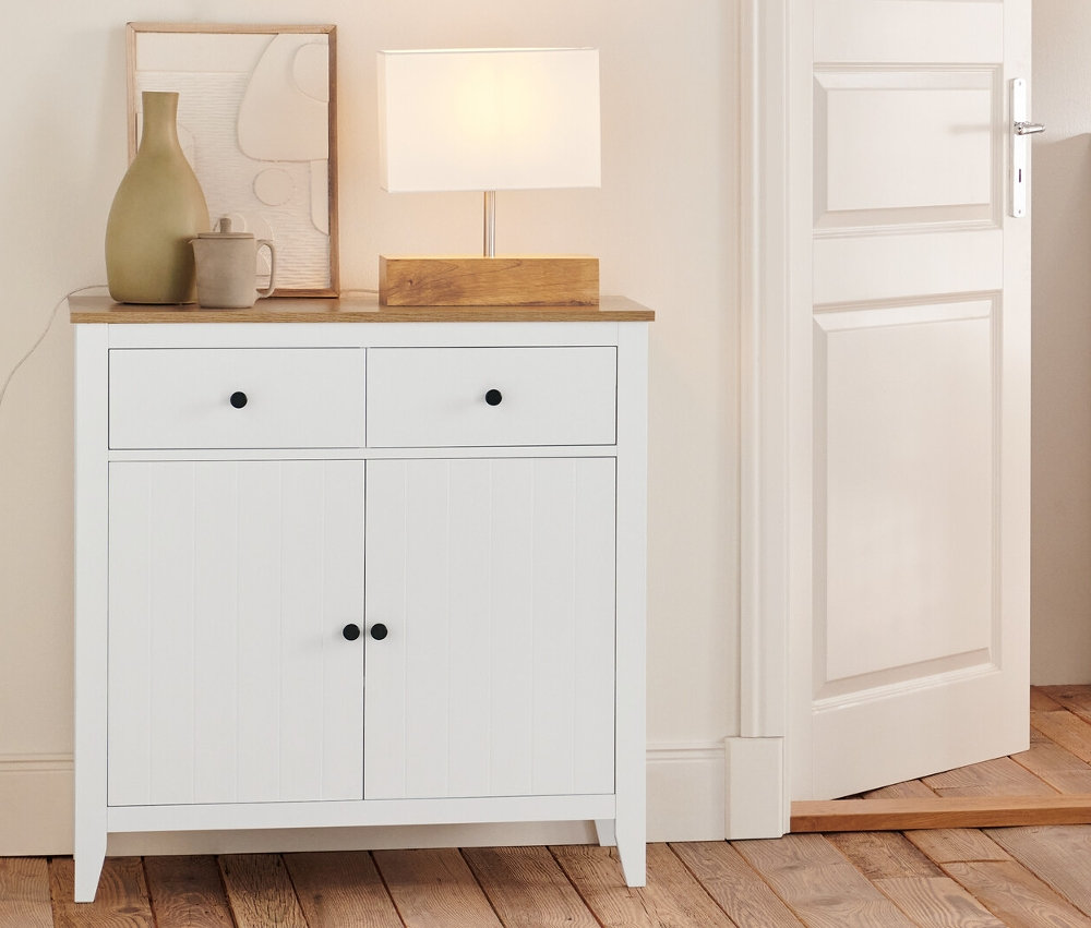 V pokoji stojí komoda se zásuvkami, odkládací skříňka, regál a lampa s dřevěným podstavcem.