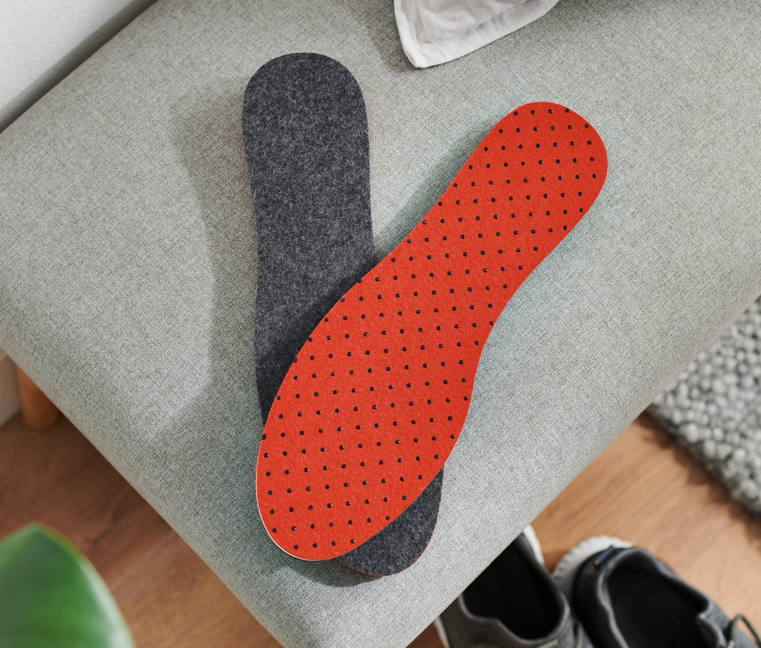 Na šedé lavici leží pár termoizolačních vložek do bot vedle sebe. Jedna je šedá, druhá červená s černými puntíky. Pod nimi jsou šedé boty.