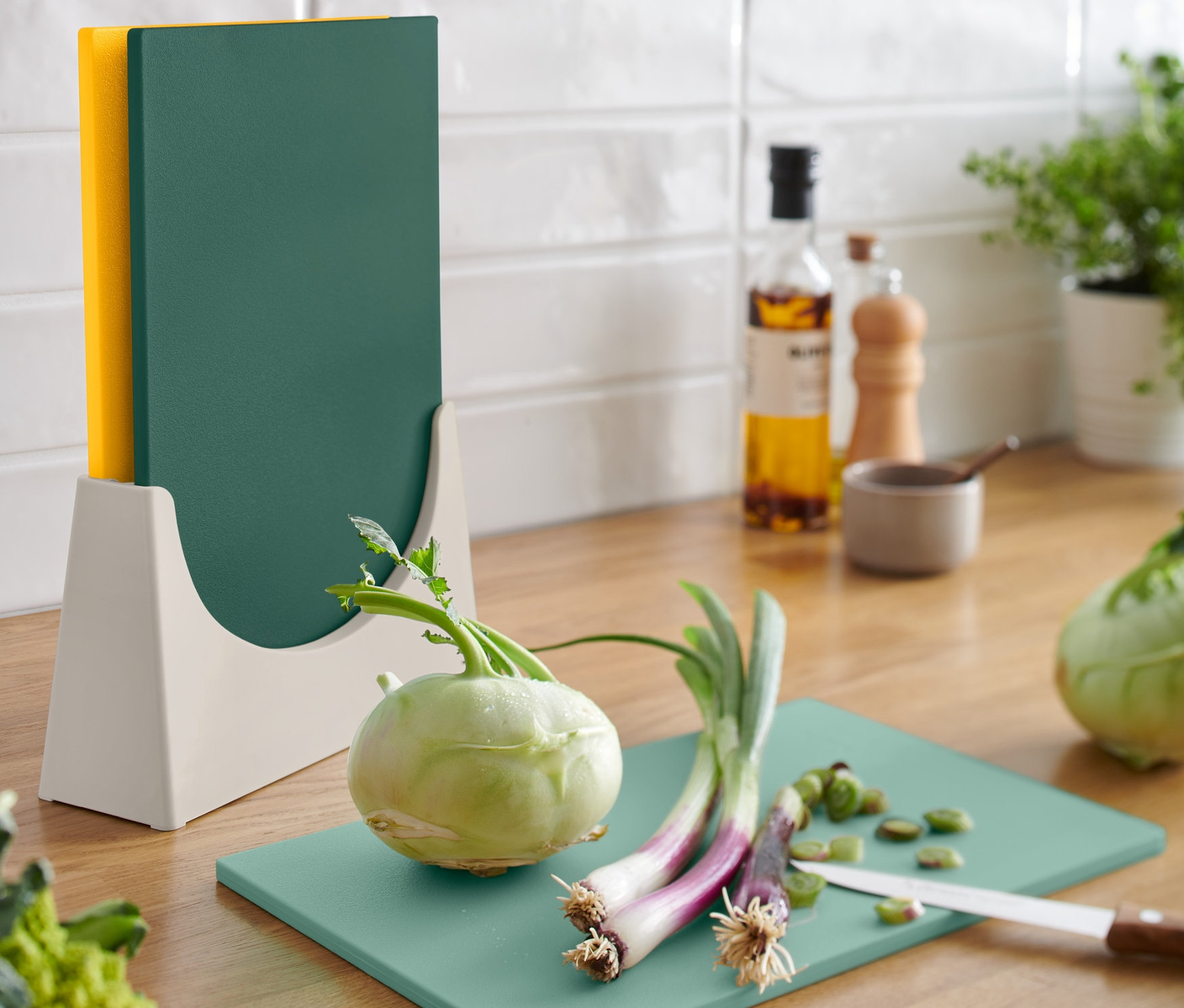 Na kuchyňské lince stojí stojan s třemi krájecími prkénky. Na jednom z prkének leží nakrájená zelenina.