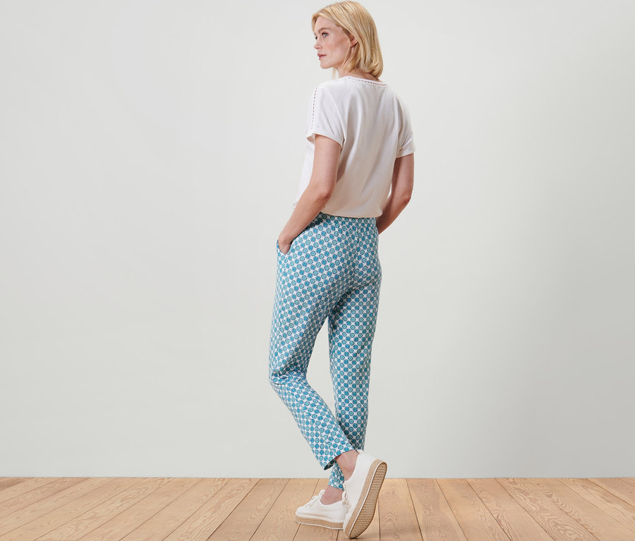 Blondýna stojí zády k divákovi a má na sobě jersey kalhoty s celoplošným potiskem.