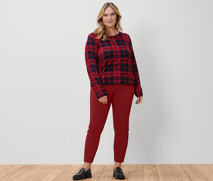 Žena stojí a má na sobě kostkované halenkové triko, červené strečové kalhoty a kožené mokasíny.