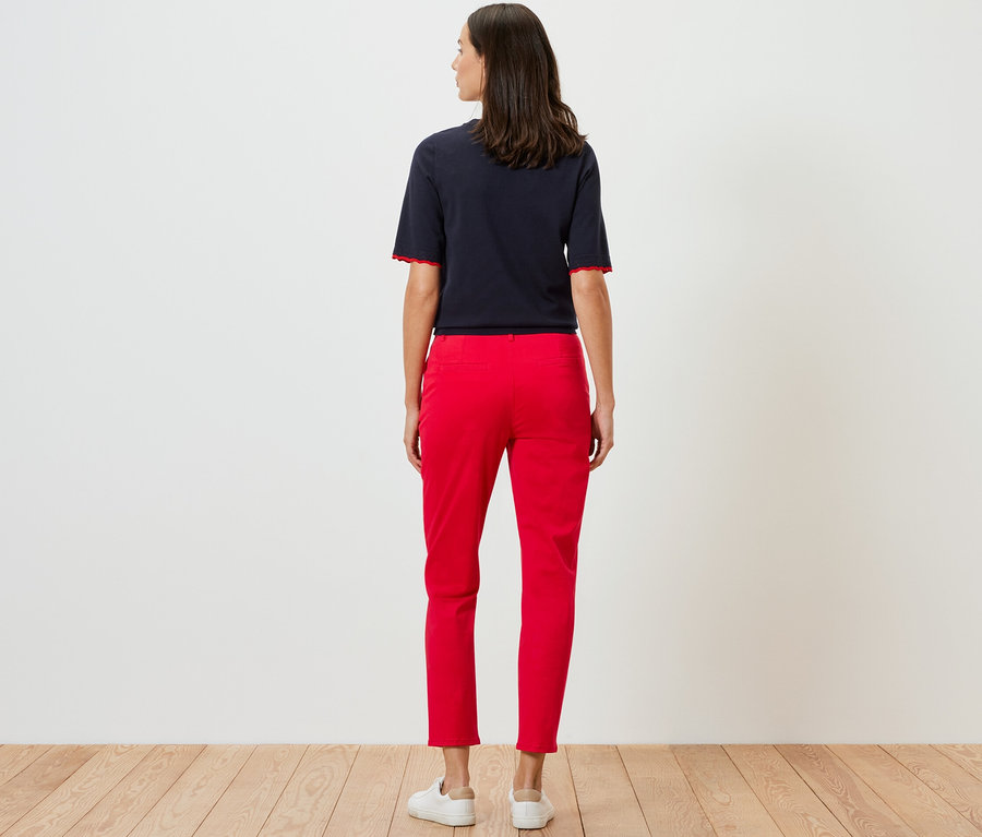 Žena pózuje zády v červených kalhotách chino.