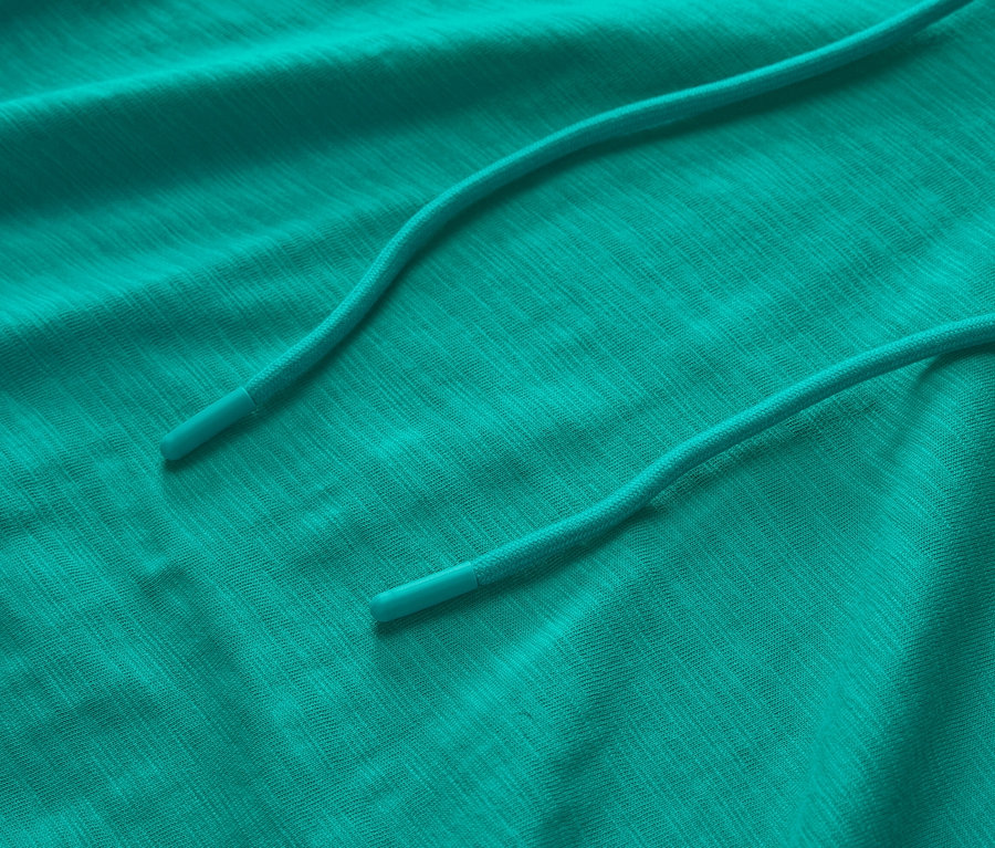 Detailní záběr tyrkysové žerzejové mikiny s kapucí a stahovací šňůrkou.