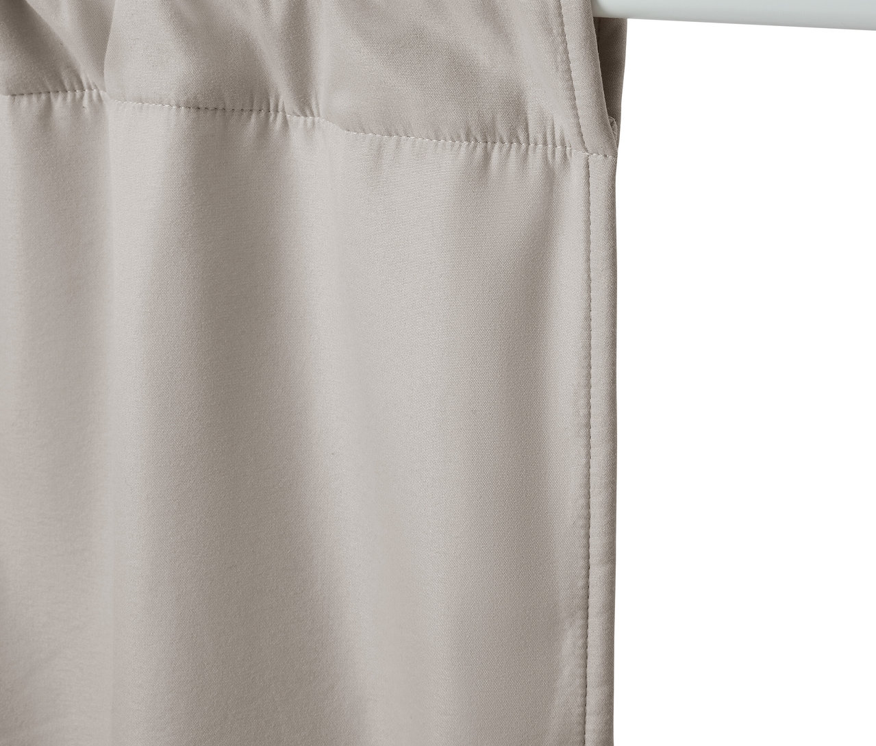 Béžový závěs visí na bílé tyči.