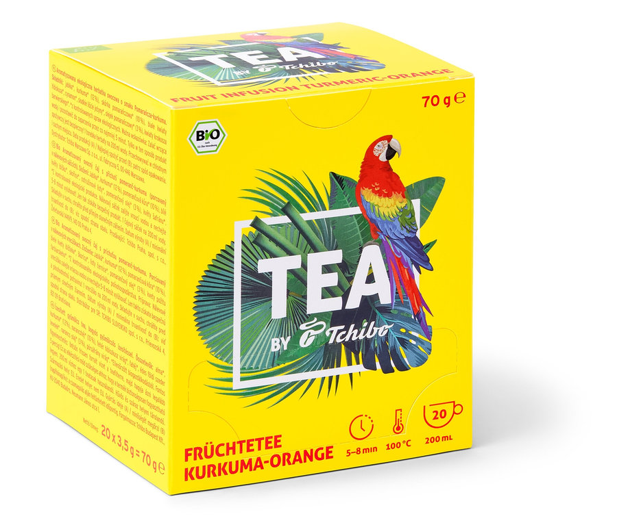 Žlutá krabička čaje TEA by Tchibo s příchutí kurkuma/pomeranč, s obrázkem papouška a tropických listů.