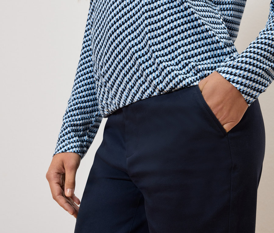 Částečný pohled na osobu s rukou v kapse kalhot a na sobě modrobílý top.