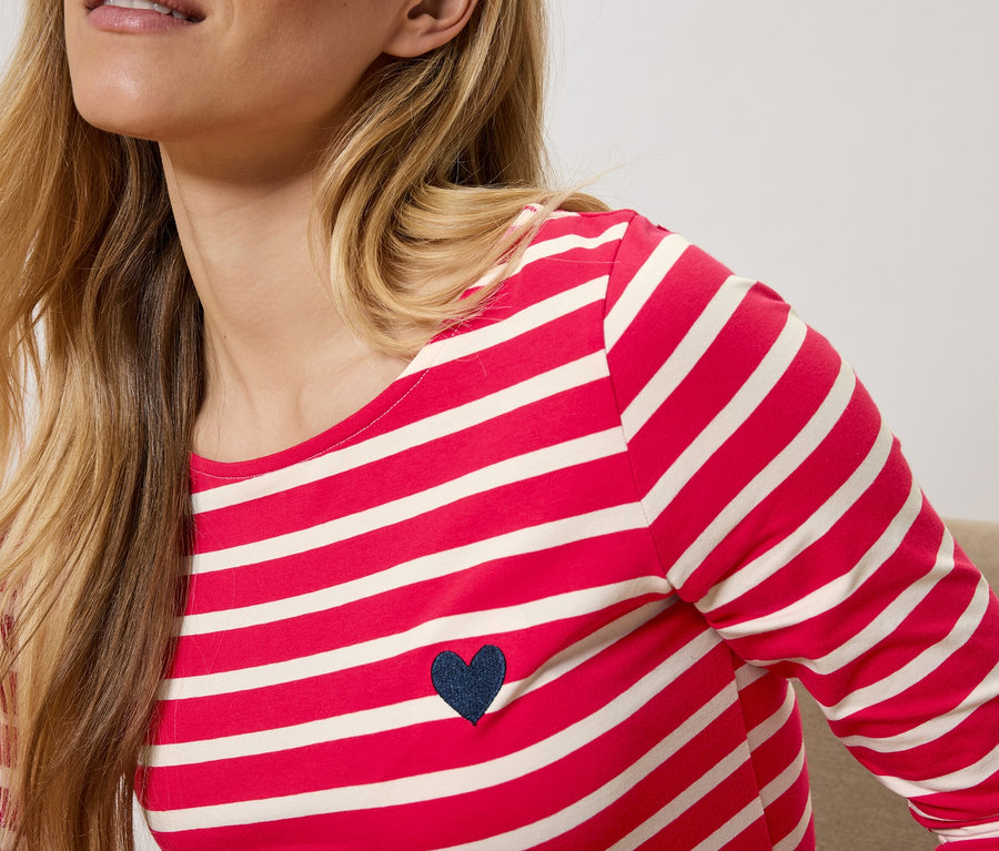 Blondýna má na sobě červeno-bílé pruhované tričko s dlouhým rukávem a tmavě modrým srdíčkem.