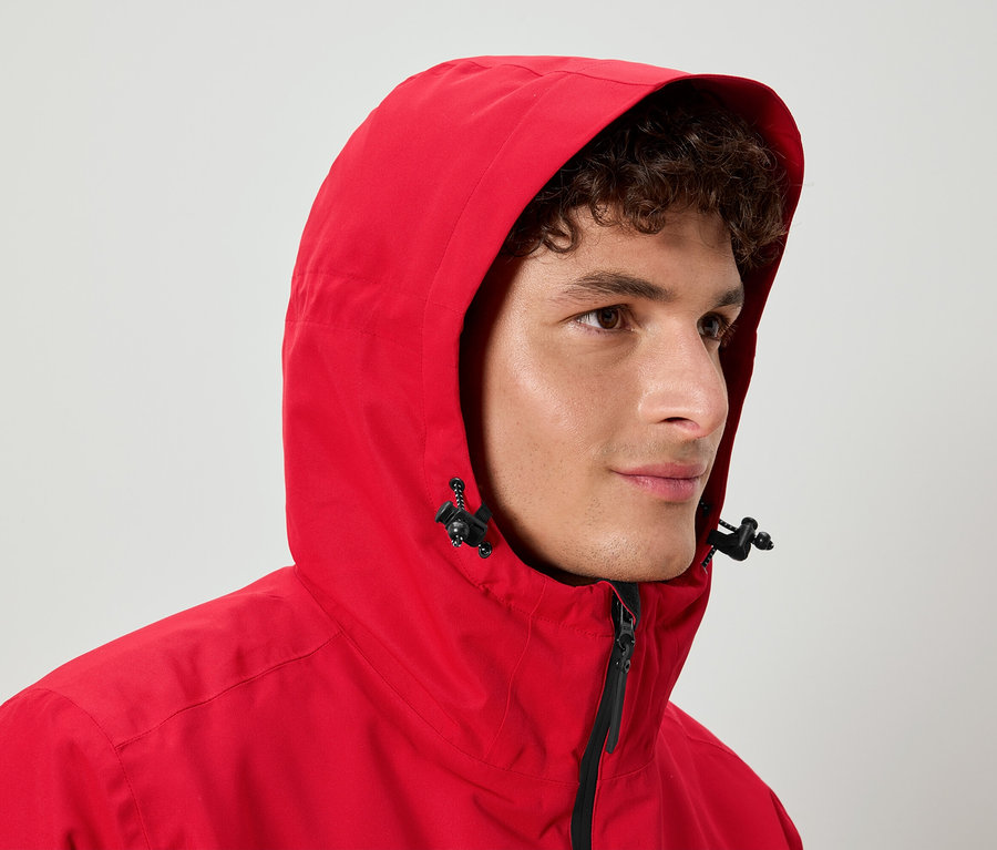 Muž s kudrnatými vlasy má na sobě červenou bundu s kapucí.